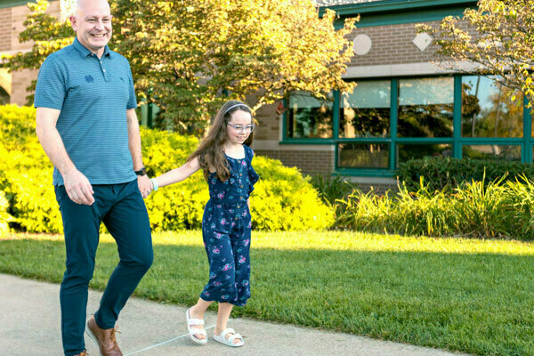 A father and daughter walking hand-in-hand outside of a school.