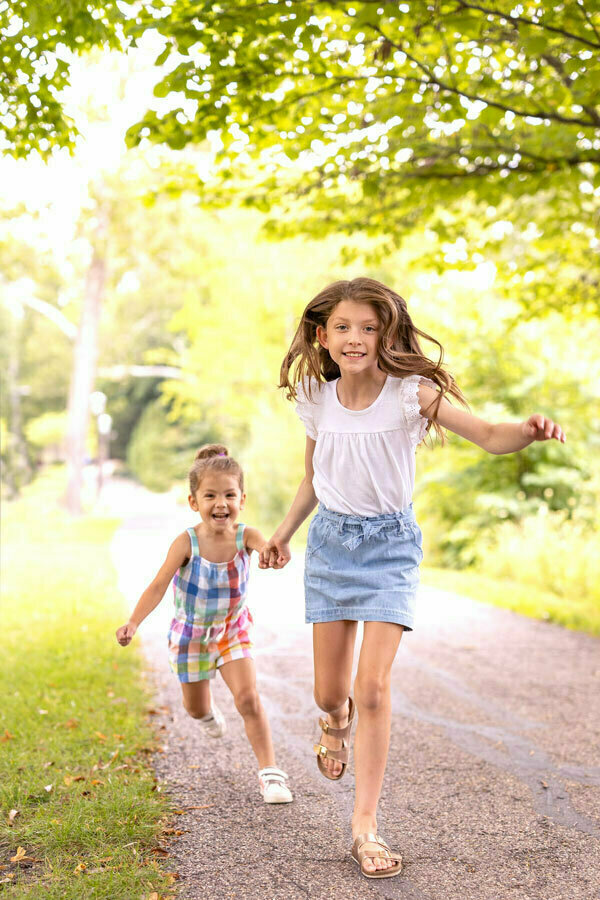 Two young girls holding hands and running down a path while looking at the camera.